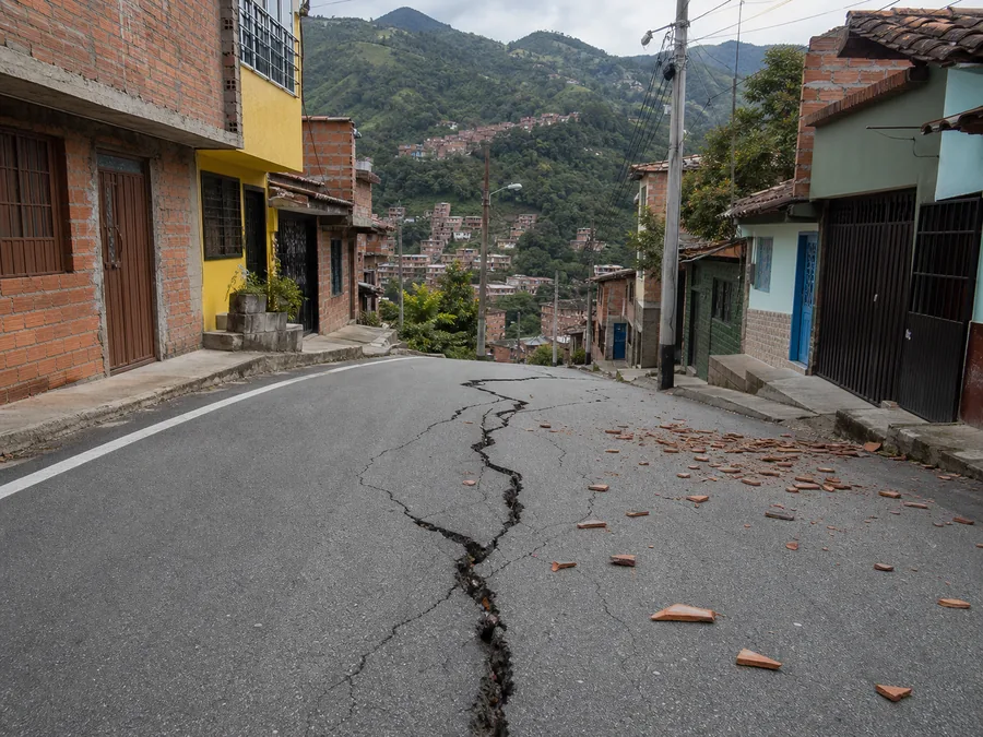 Calle de barrio con una grieta en el asfalto y edificaciones aún en pie